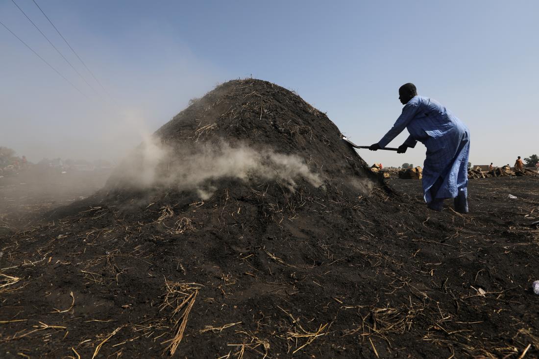 A man shovels hay o<em></em>nto a heap of stacked wood during charcoal production in Maiduguri, Nigeria October 29, 2021. Picture taken October 29, 2021. REUTERS/Afolabi Sotunde