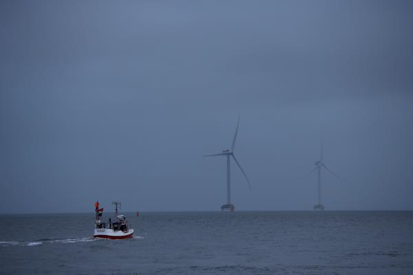 A fishing boat sails in front of wind turbines through the Thyboron Canal in Jutland, Denmark