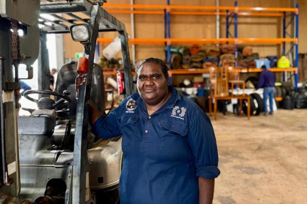 An Aboriginal woman wearing a navy work shirt holds o<em></em>nto the l<em></em>ink of a buggy in a work shed and looks at the camera