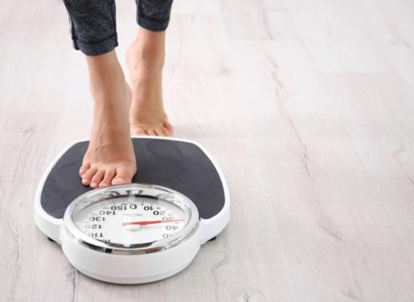 woman stepping on scale, co<em></em>ncept of how much weight to safely lose in a month