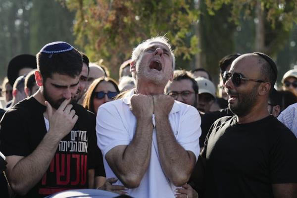 A man in a white shirt cries out, holding his fists up toward his face, as other men in black stand beside him.