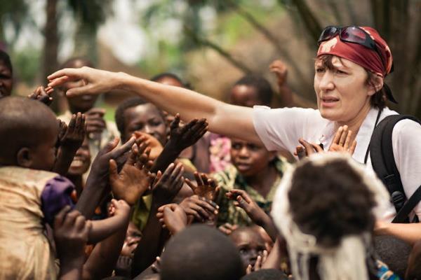 A white woman volunteer puts her hand out to a crowd of African children