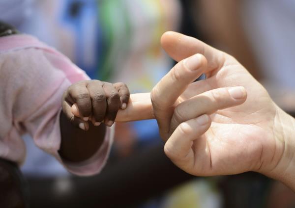 The fingers of a black child curled around one white finger