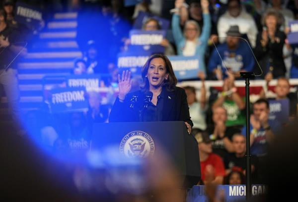 A woman speaks at a podium with a cheering crowd behind her