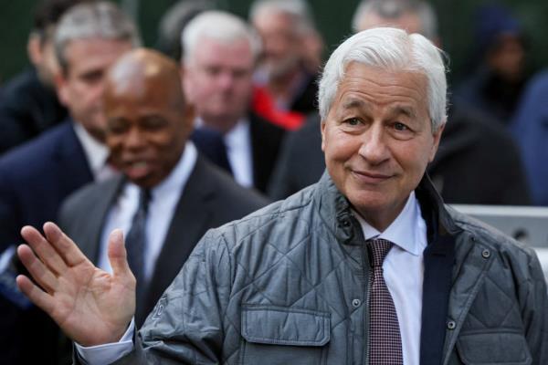 Jamie Dimon waves his hand and smirks outdoors.