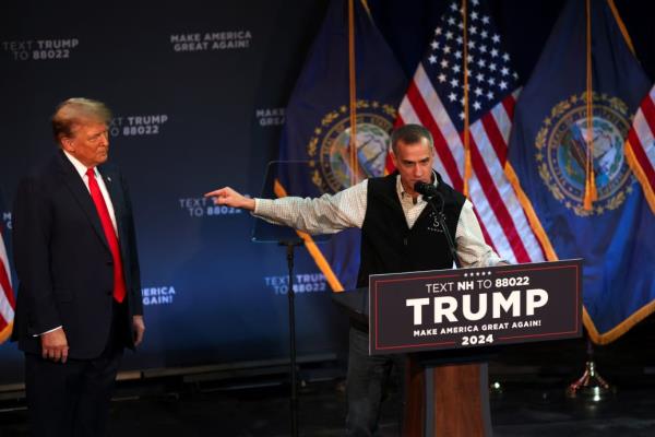 Corey Lewandowski speaks behind a podium, next to Do<em></em>nald Trump