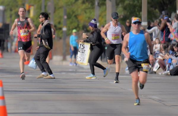 Two spectators cross between runners who head for the finish line during the 24th Annual Running Festival at the inner harbor. (Karl Merton Ferron/Staff)