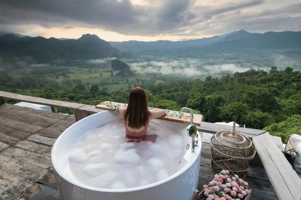 A woman relaxes in a giant outdoor bath while overlooking a green landscape, in a scene depicting luxury travel.