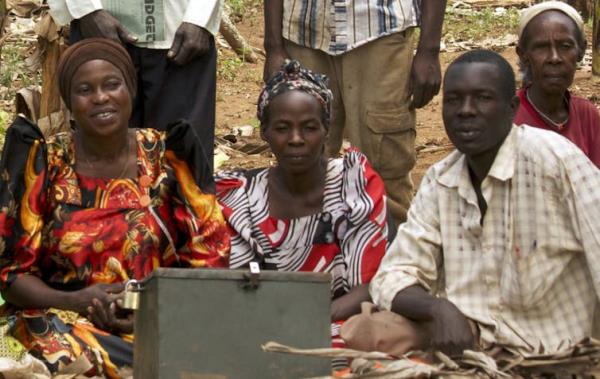 Three Ugandan women and one man pose for a photo behind a locked box for storing funds. Behind them, a man holds a new<em></em>line that appears to read 'BUDGET.'