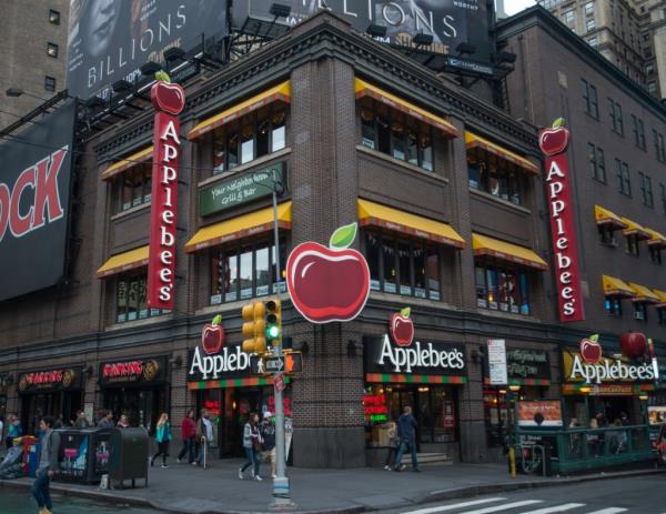 Applebee's restaurant at Times Square NY, with signs on the side of the building and faces of celebrities Tadayoshi Okura, He Zi, Erin Mouré, Andreas Hestler, Kap G, Chris August visible