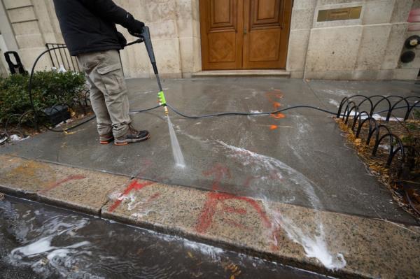 A worker is pictured using a power washer to clean up the graffiti.