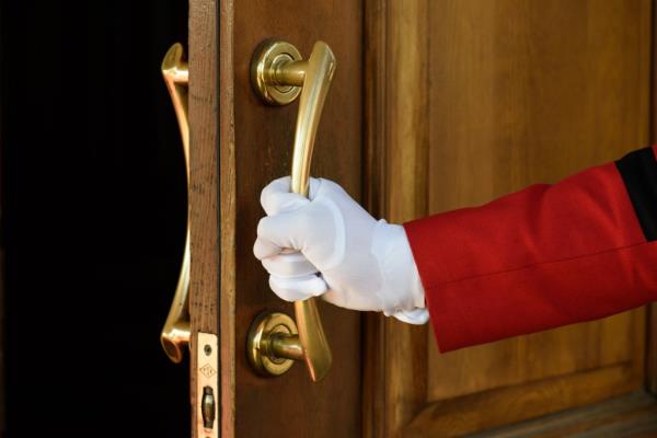 Gloves hand opening a wooden door with an ornate handle