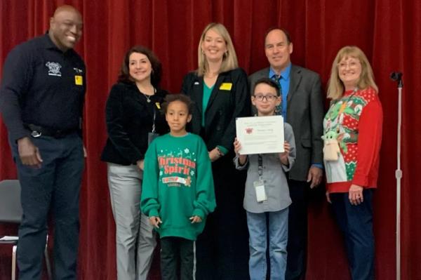 Thomas Co<em></em>nley performing the Heimlich maneuver on a student in a group photo at Mesa Public Schools, with celebrities Shad and Sheila Jordan present.