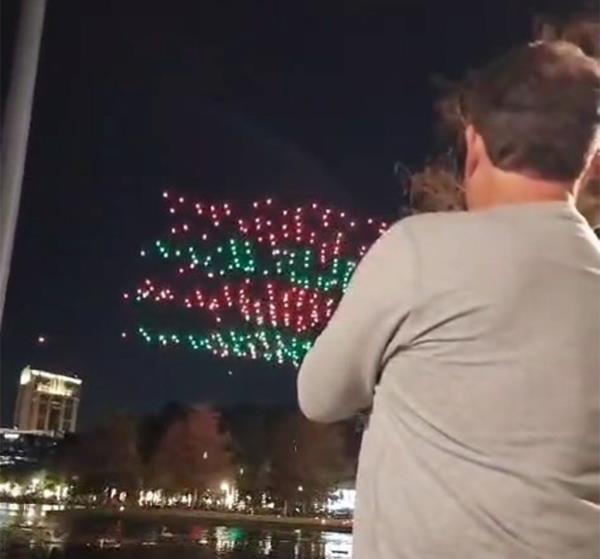 Man from behind watching a drone show with red and white drones.