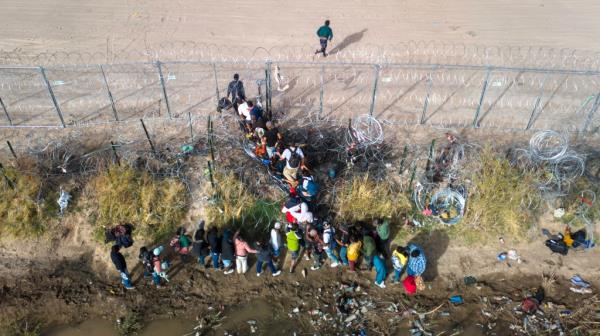 migrants pass through coils of razor wire while crossing the U.S.-Mexico border