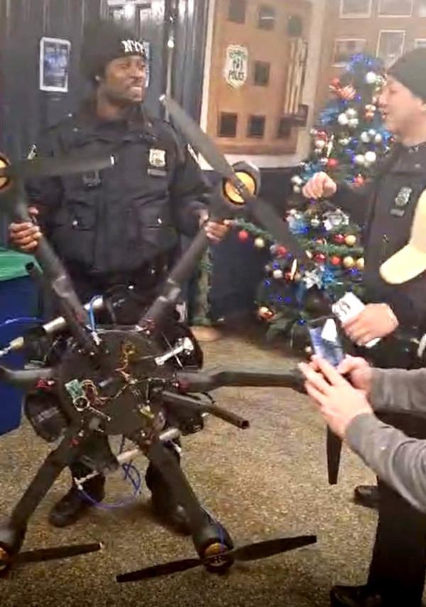 NYPD officer smiling as he holds up a large black drone