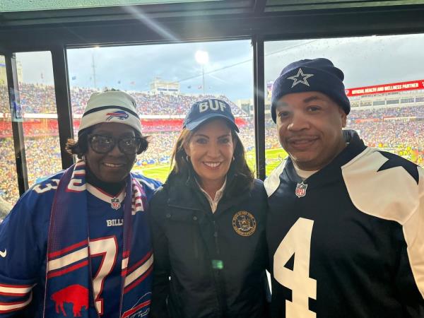 Governor Hochul in a suit at a Bills games standing in the middle of Majority Leader Crystal People-Stokes and Assembly Speaker Carl Heastie.