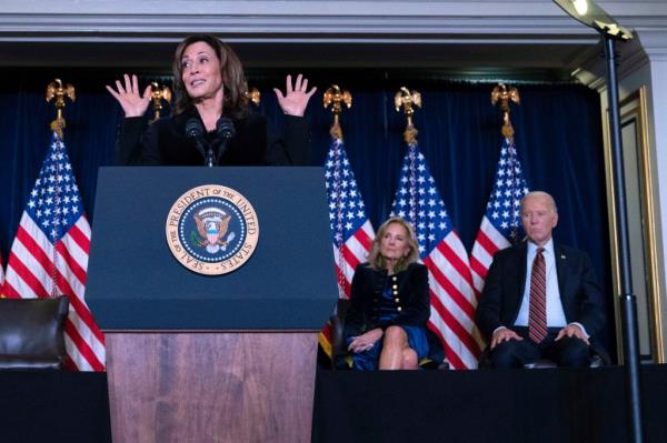 Vice President Kamala Harris speaking at podium, with President Joe Biden and First Lady Jill Biden attentively listening, at the Democratic Natio<em></em>nal Committee's Holiday Reception.